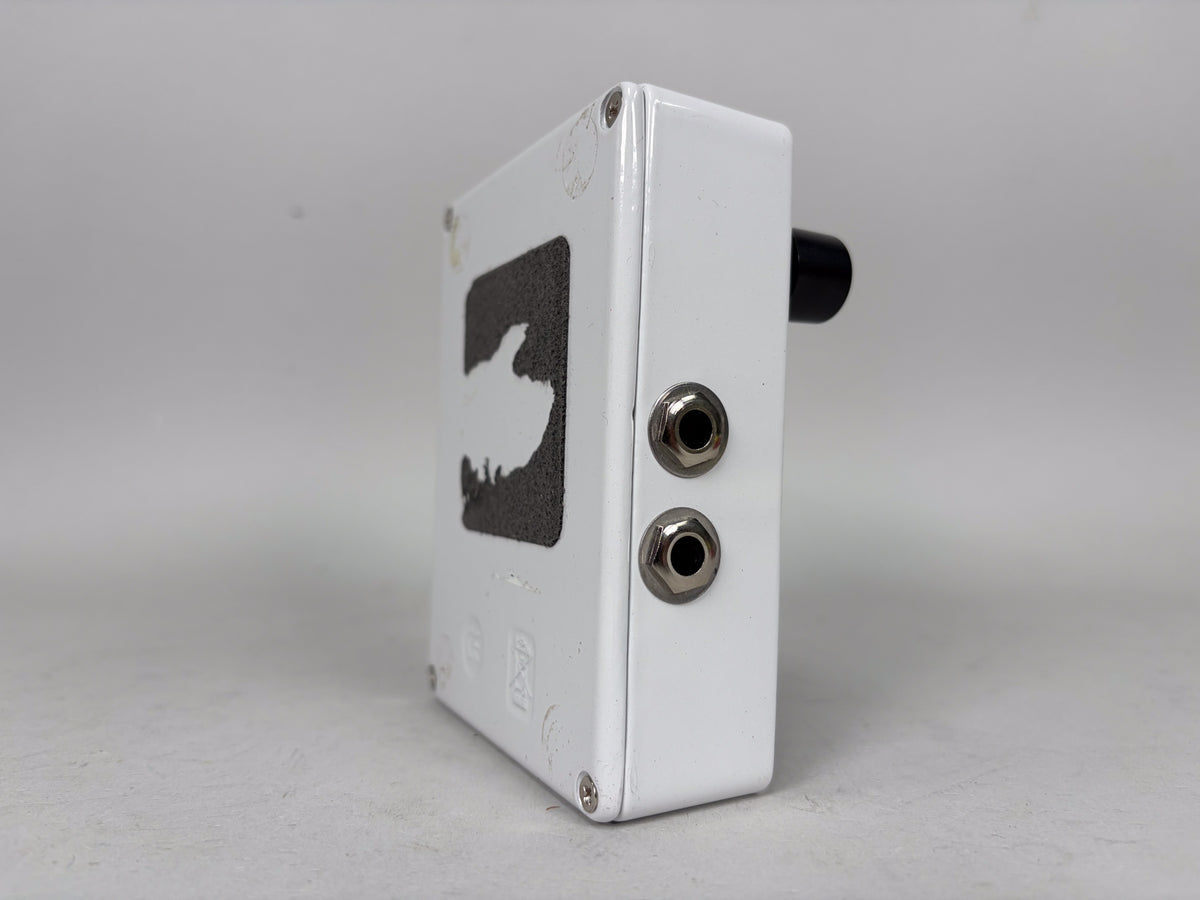 The white pedal is viewed from the right side, showing two input jacks and a black knob, with a textured dark gray logo on the top.