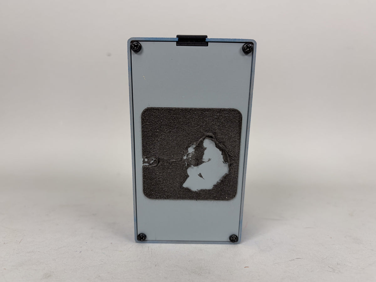 The light blue pedal's bottom is shown, with a large, worn black rubber pad covering most of the surface.