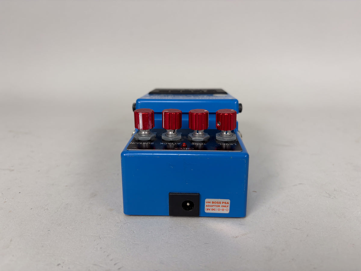 Blue Boss CS-3 pedal with red knobs for Sustain, Attack, Tone, and Level, and a 9V DC adaptor label.