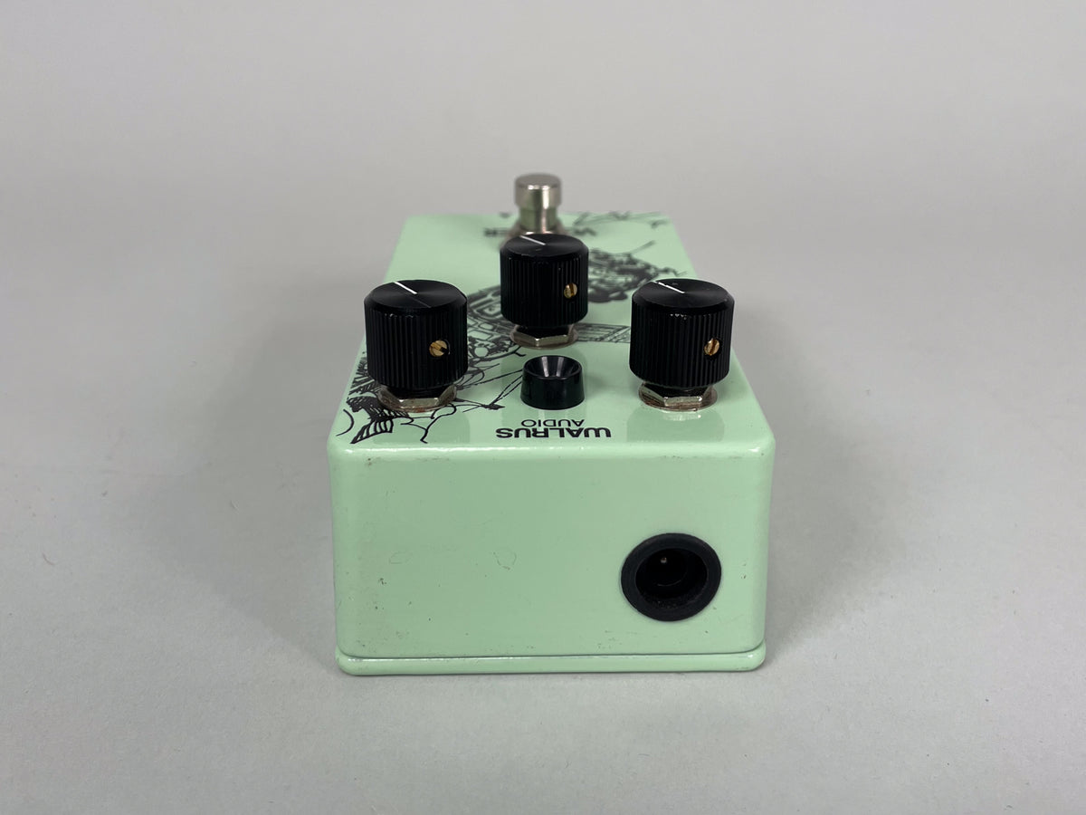 The mint green pedal is viewed from the right side, showing a black input jack and three black control knobs.