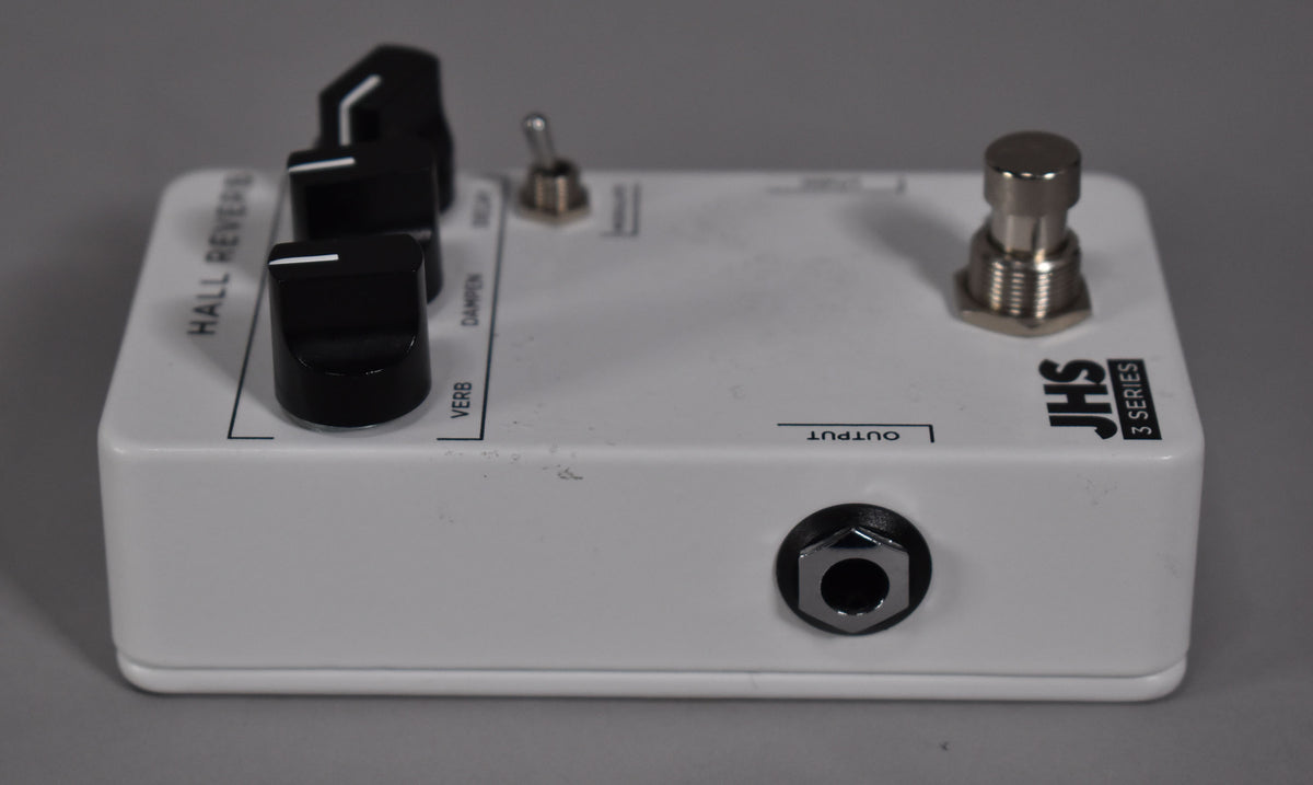 A white guitar pedal with black knobs and a chrome footswitch, viewed from the upper right, showing the output jack.