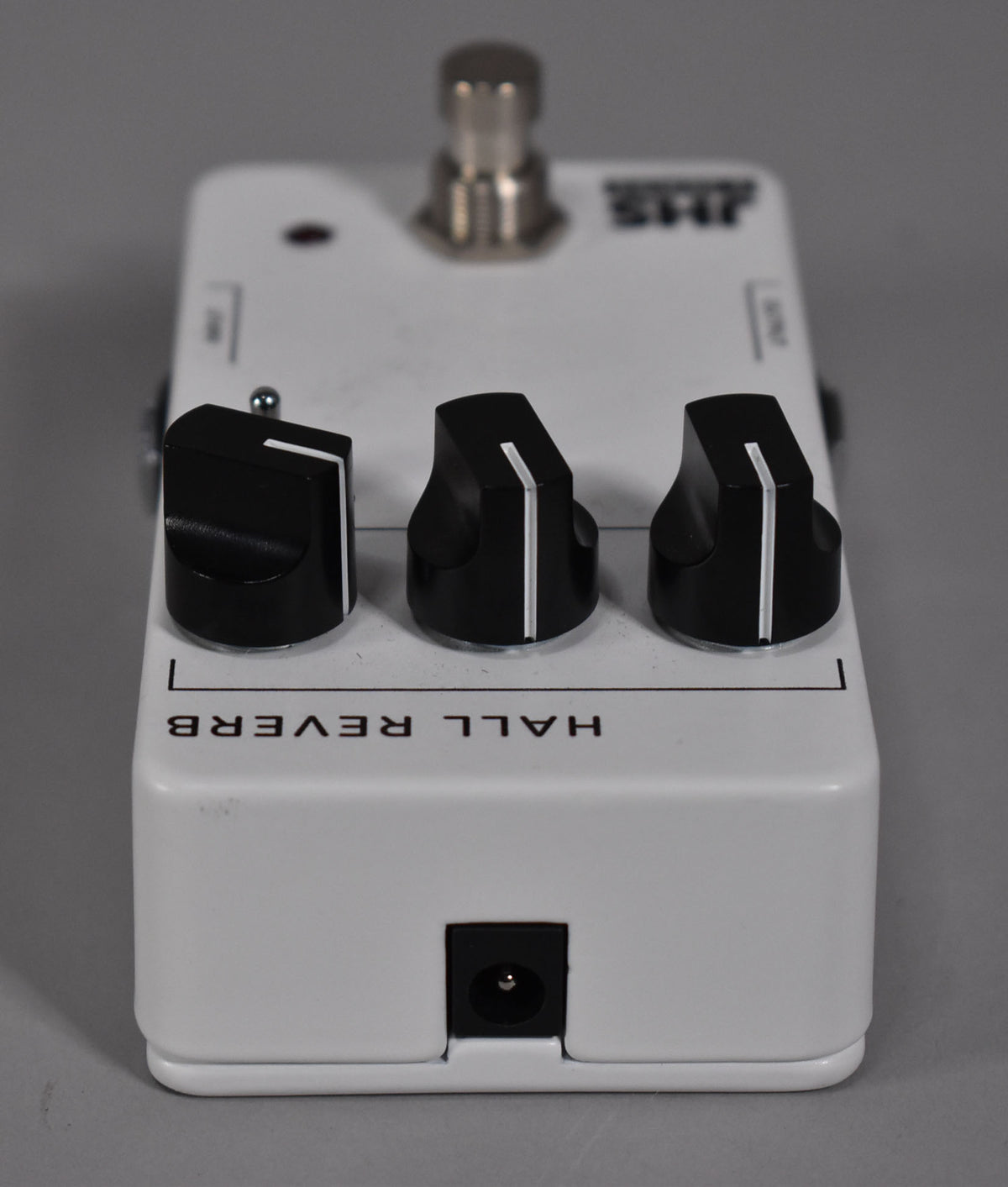 A white guitar pedal with three black control knobs, each with a white indicator line, viewed from a low angle showing the front edge with a power input.