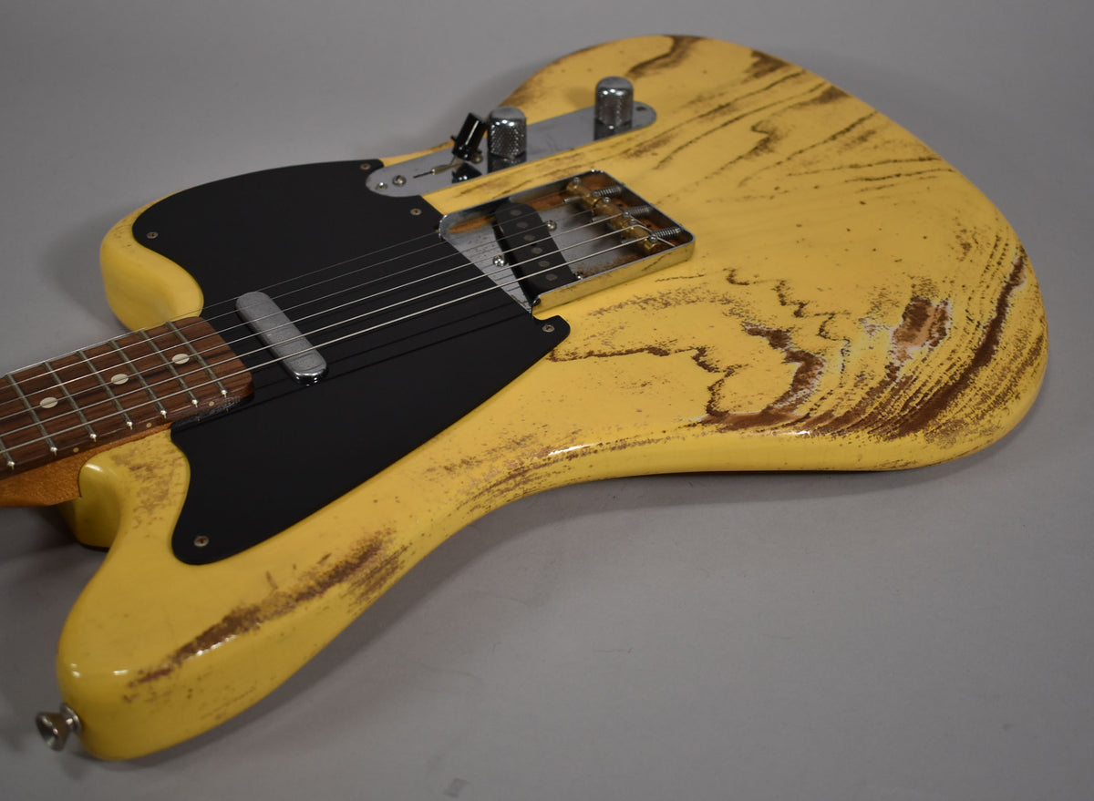 The butterscotch blonde guitar body, with heavy brown relic wear, is angled from the lower bout towards the neck, showing a black pickguard.