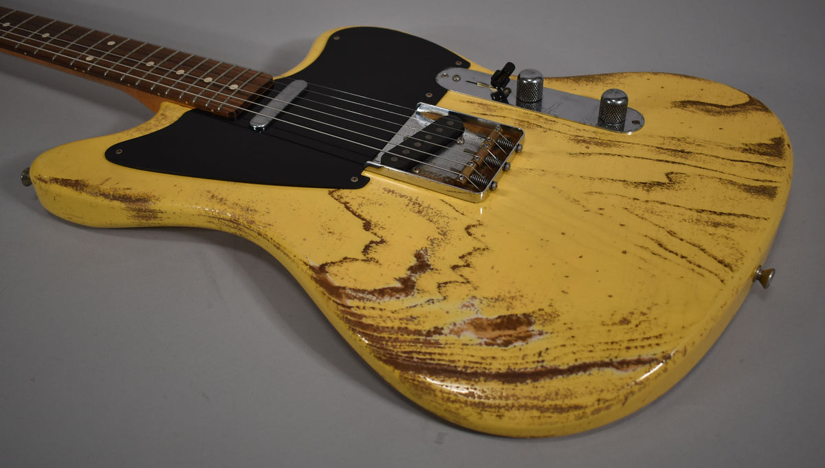 The butterscotch blonde guitar body, with heavy relic wear and a black pickguard, is angled from the neck toward the lower bout.