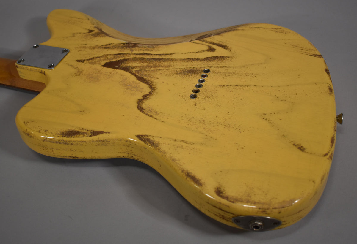 The guitar's butterscotch blonde back shows heavy relic wear, a chrome neck plate, six string-through-body ferrules, and an output jack.