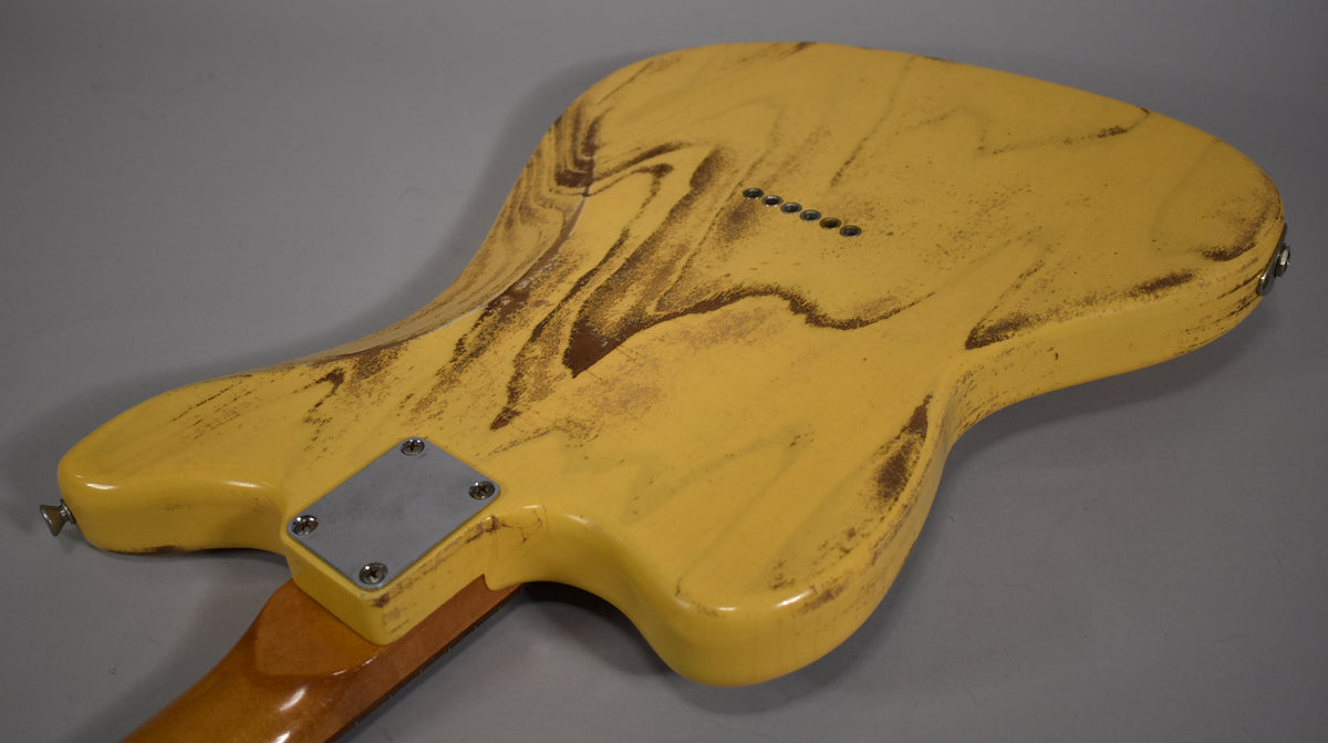 The back of a butterscotch blonde electric guitar, heavily distressed with dark brown wear, showing six string-through-body ferrules.