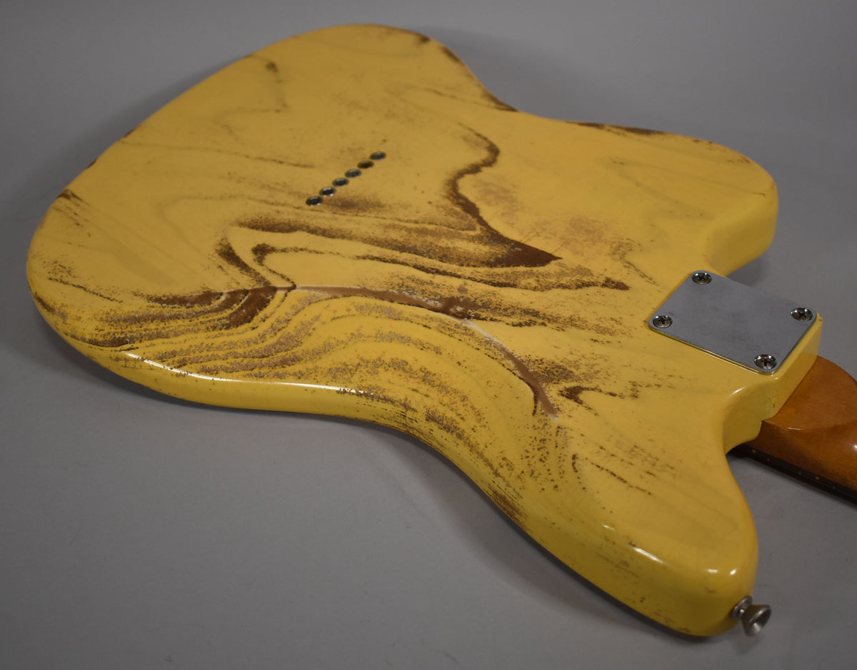 The back of a distressed butterscotch blonde guitar body, showing wood grain and relic'd brown wear, with a chrome neck plate.
