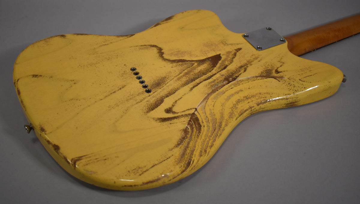 The back of a distressed butterscotch blonde guitar body with a visible wood grain, six string-through ferrules, and a neck plate.
