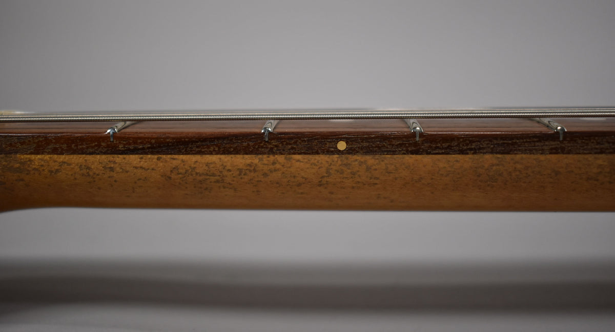 Close-up of the guitar neck's side, showing the dark fretboard, frets, strings, and a single round fret marker on the worn, butterscotch-blonde neck.