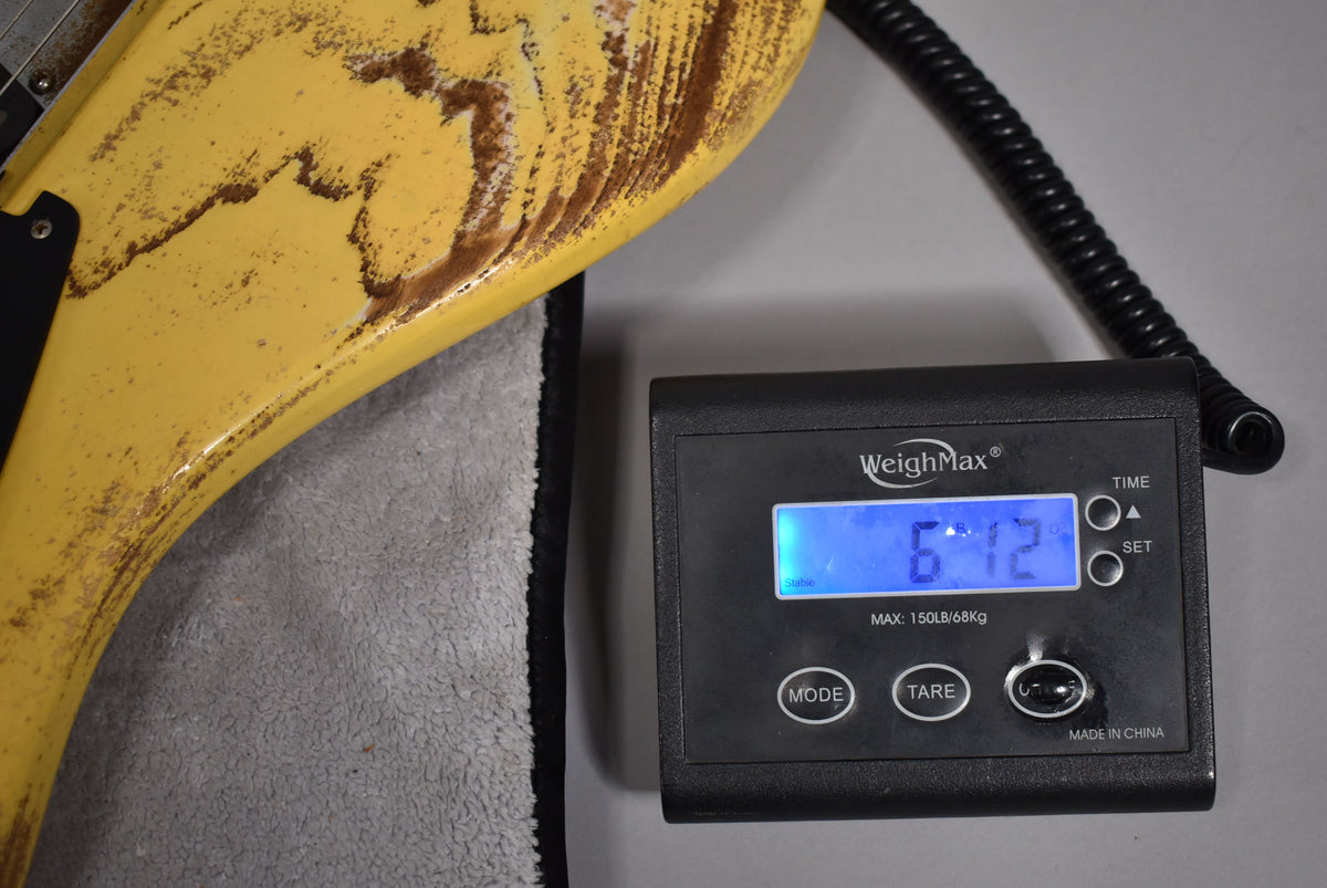 The guitar's distressed butterscotch blonde body with heavy brown relicing rests on a scale displaying "6.12" pounds.