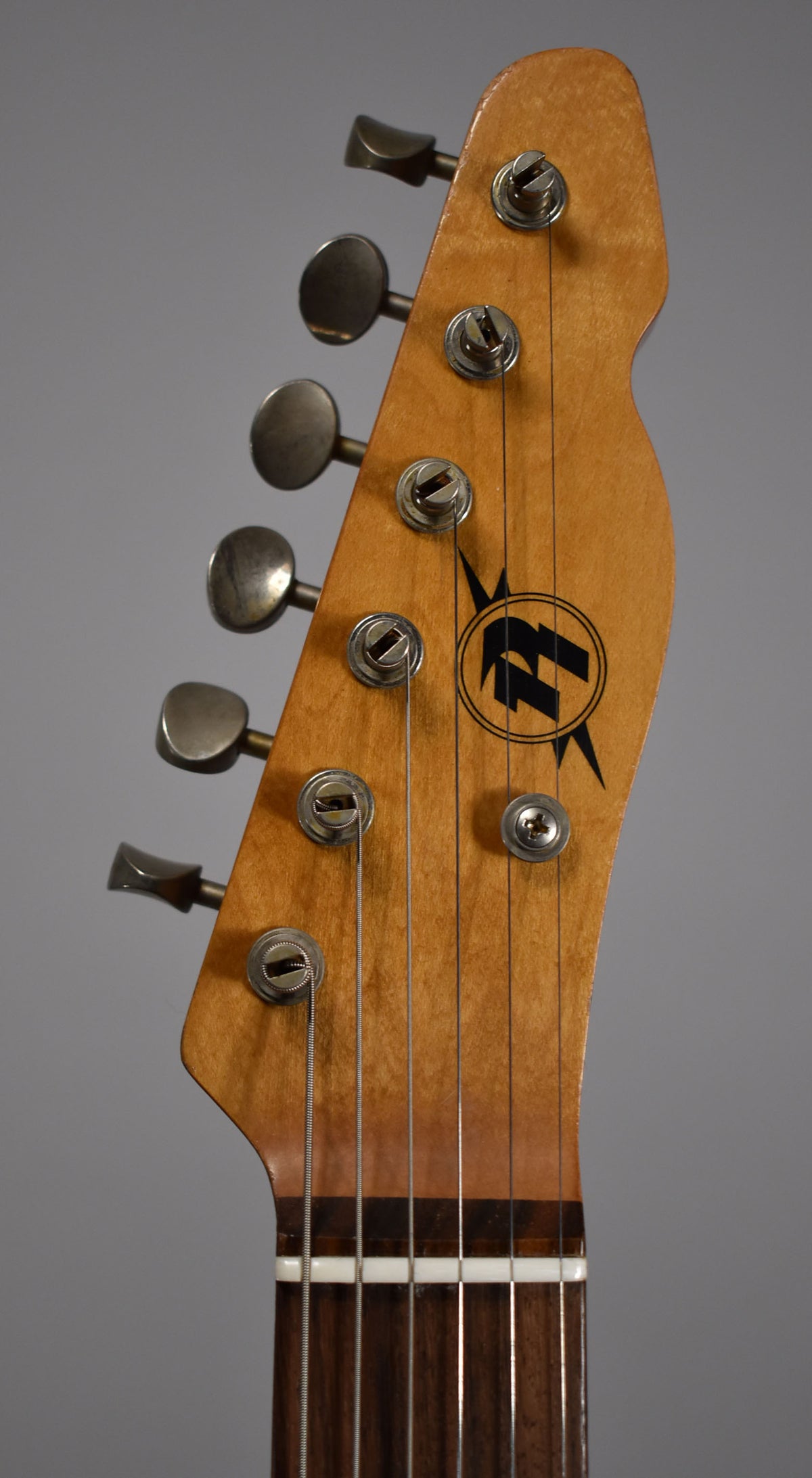 The butterscotch blonde headstock, angled left, features six aged nickel tuners and a dark brown fretboard with a white nut.