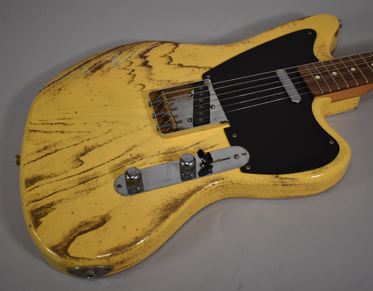 The butterscotch blonde guitar body, with heavy relic wear and a black pickguard, is angled from the lower bout.