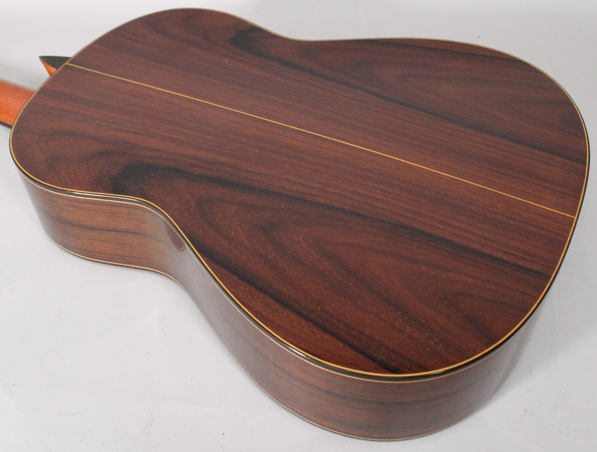 The classical guitar's dark reddish-brown back and sides, with a visible wood grain and light binding, are angled from the lower bout.
