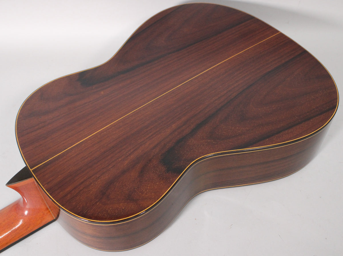 The classical guitar's dark reddish-brown back and sides feature a prominent grain, with a light wood stripe down the center.