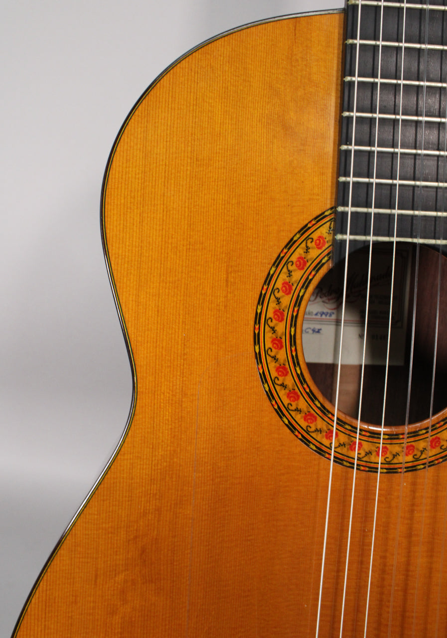 Close-up of the classical guitar's upper bout, showing the light-colored spruce top, rose-patterned rosette, and dark fretboard.