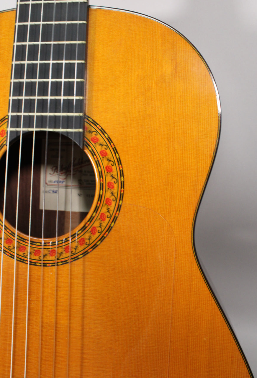 Close-up of the classical guitar's light brown body, showing the soundhole's rose rosette, fretboard, and a visible crack on the lower bout.