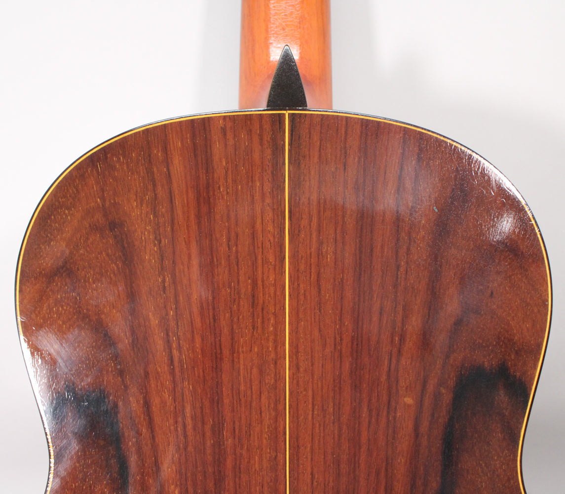 The guitar's dark brown, glossy back shows a central seam, light binding, and some surface scratches near the upper bout.