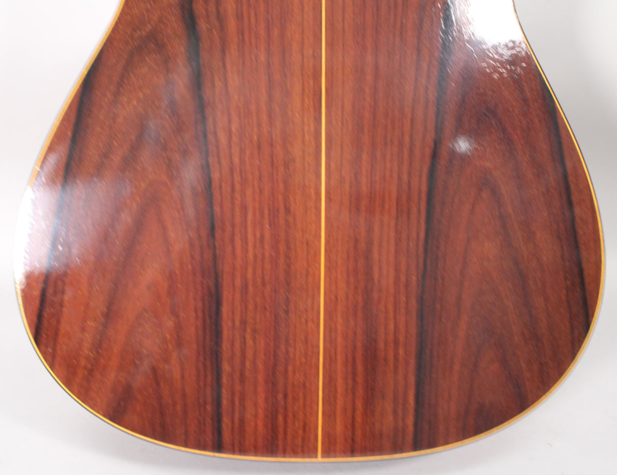 The guitar's glossy dark reddish-brown back shows prominent wood grain, a light center strip, and some light surface wear.