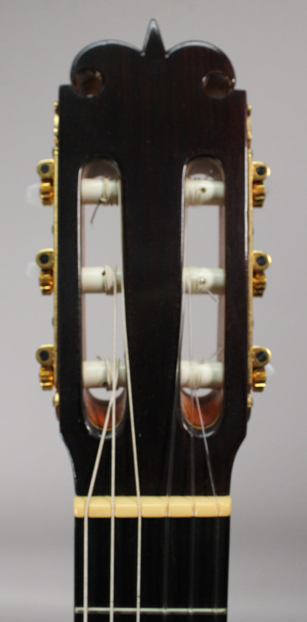 Close-up of the dark brown headstock, showing gold tuners with white buttons, white strings, and a cream-colored nut.