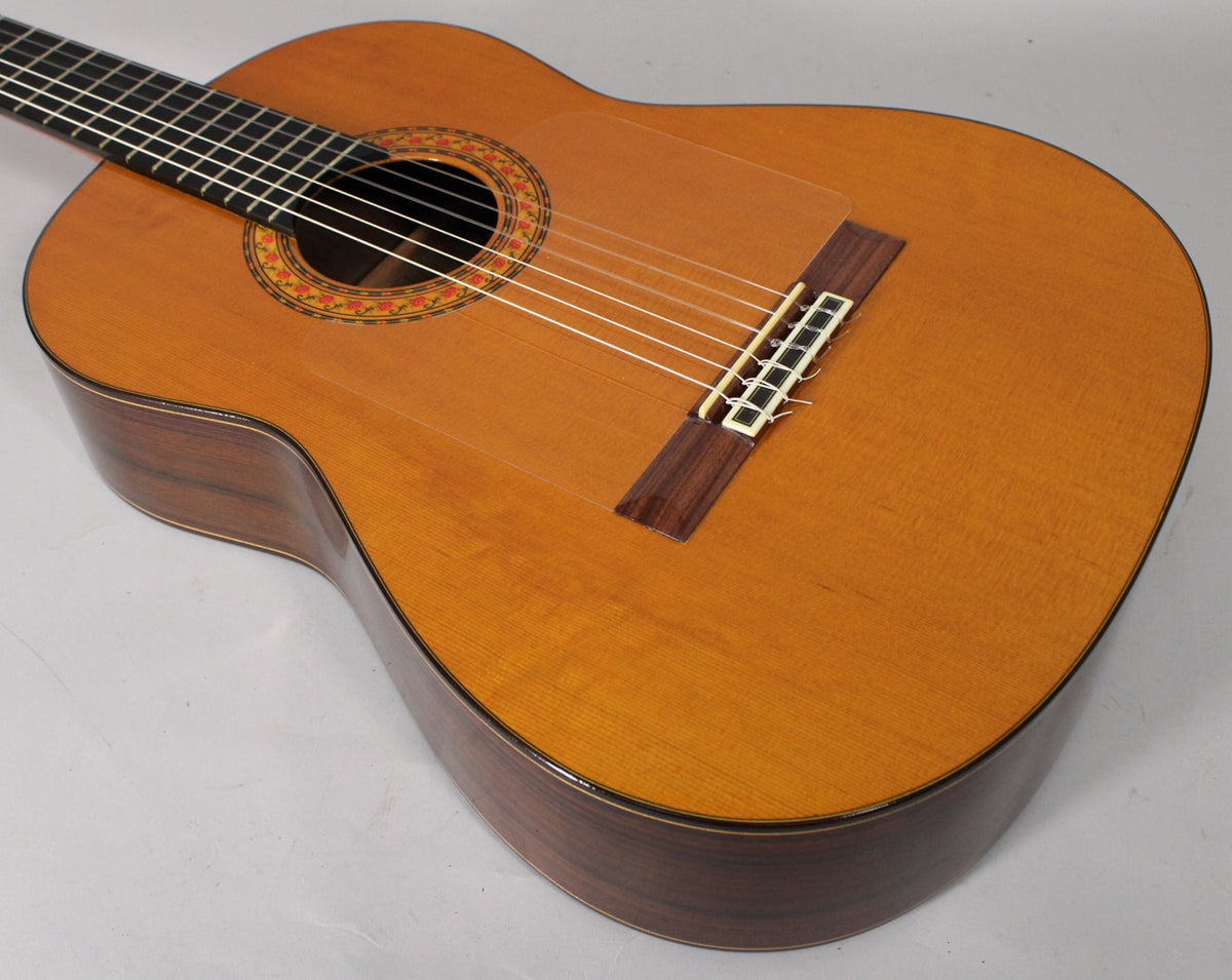 The classical guitar's body is angled, showing its light brown top, dark wood sides, and a decorative rosette around the soundhole.