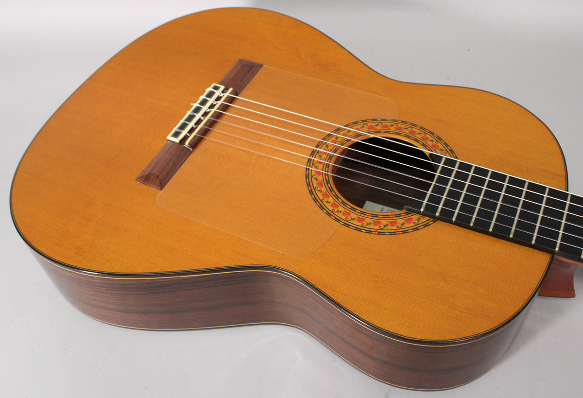 The classical guitar's light-colored top, dark wood sides, and decorative soundhole are visible from an upper-right angle.
