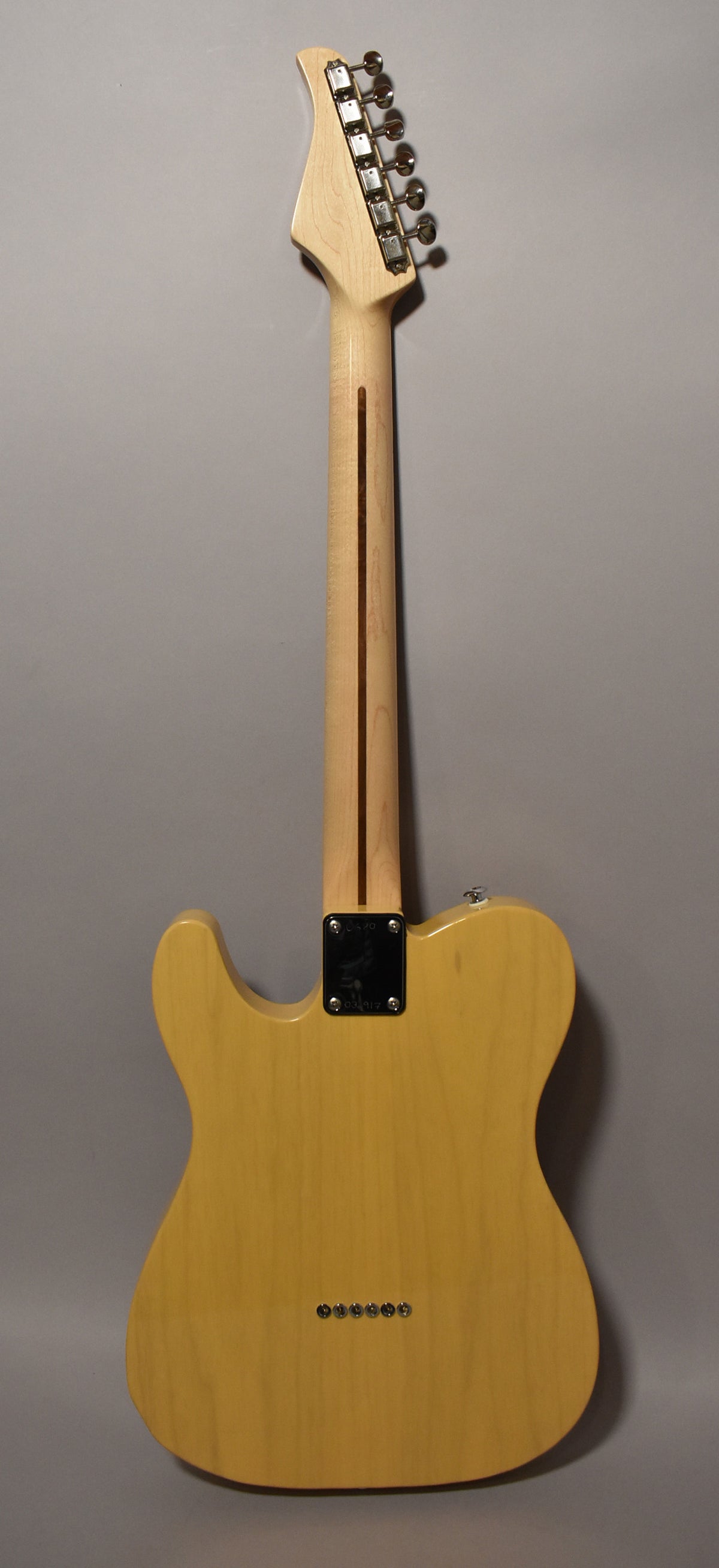 The back of a butterscotch T-style guitar, showing a light maple neck, chrome tuners, and string-through-body ferrules.