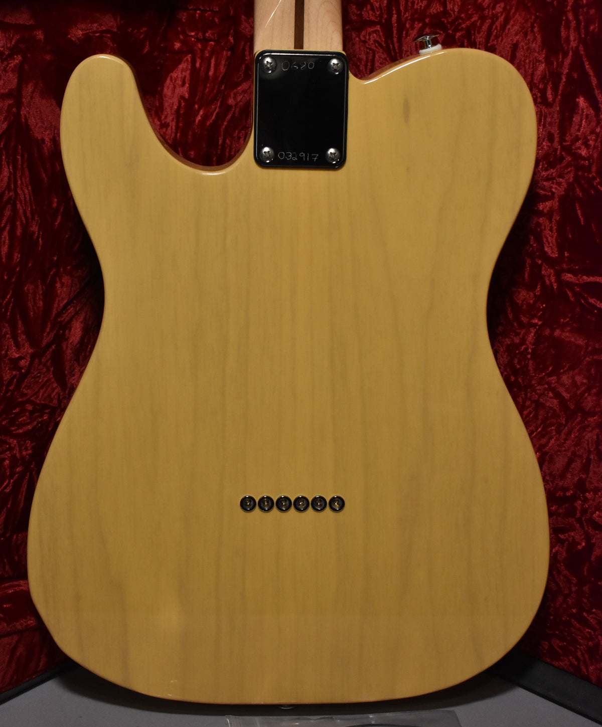 The back of a butterscotch T-style guitar shows string-through-body ferrules, a neck plate, and a strap button, with minor wear.