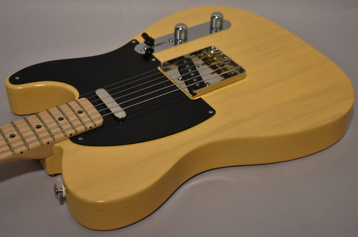 The butterscotch T-style guitar's body, black pickguard, and maple neck with black dot inlays are visible from the lower bout.