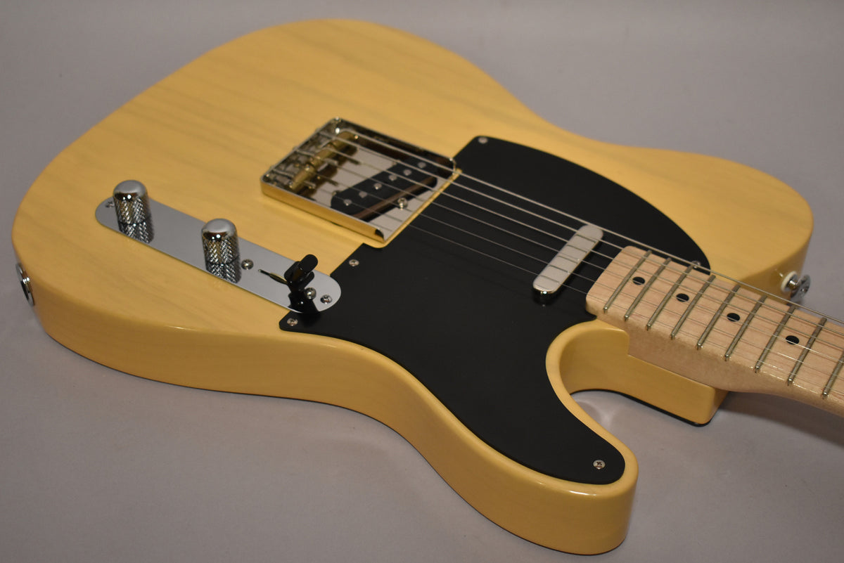 The butterscotch T-style electric guitar is angled from the upper right, showing its black pickguard, chrome bridge, and control plate.