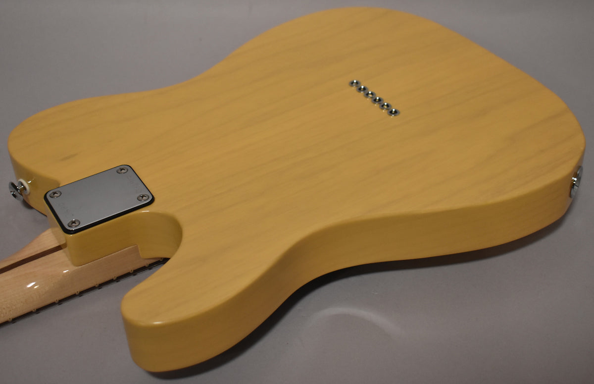 The butterscotch guitar's back shows a chrome neck plate, six string ferrules, and a light maple neck with a dark fretboard.
