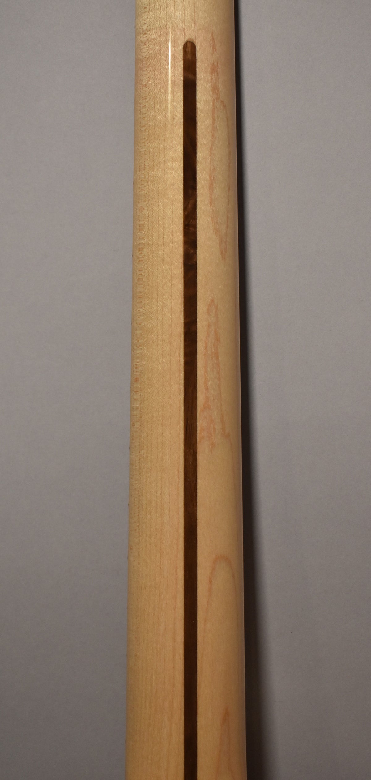 The back of a light-colored wooden guitar neck, with a dark wood stripe running down its center.