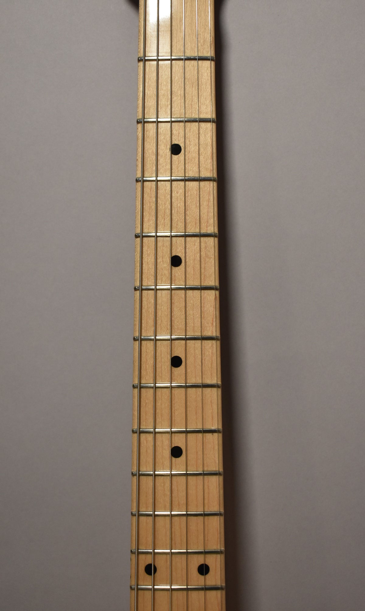 The maple fretboard, with black dot inlays and shiny frets, is shown from the 1st to the 12th fret, angled slightly left.