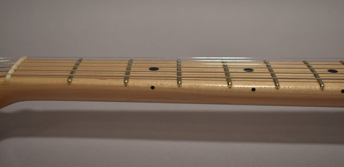 Close-up of the light maple fretboard and neck, showing black dot inlays and a white nut, with light string wear.
