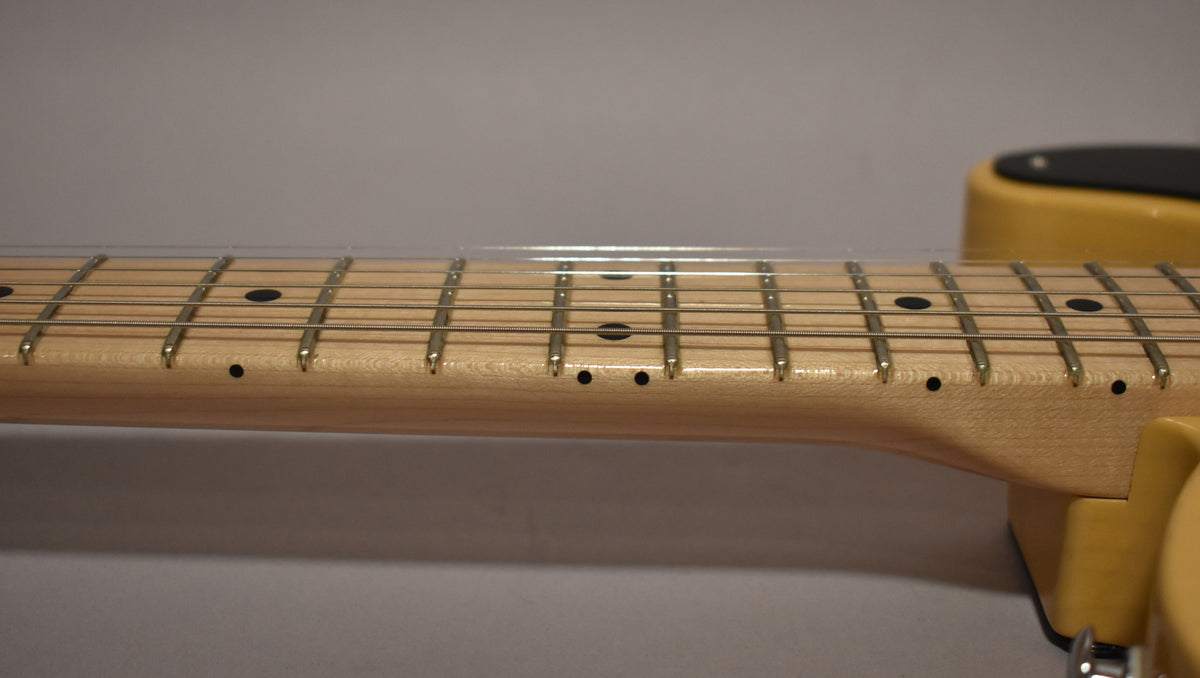 Close-up of the light maple fretboard and frets, with black dot inlays and side markers, and a butterscotch body visible right.