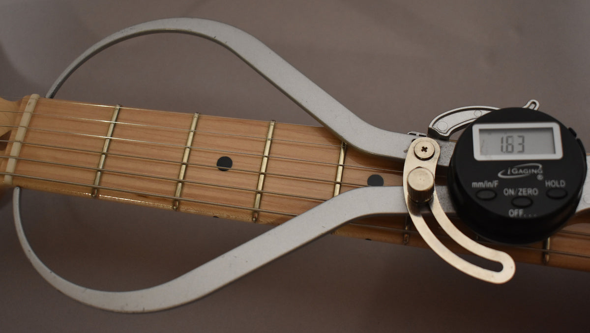 A digital string action gauge measures the height of the strings above the light maple fretboard, displaying "1.63".
