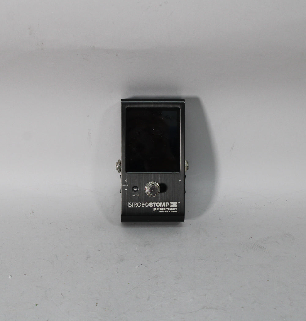 A dark gray, brushed metal tuner pedal with a large black screen and a single chrome footswitch, viewed from the front.