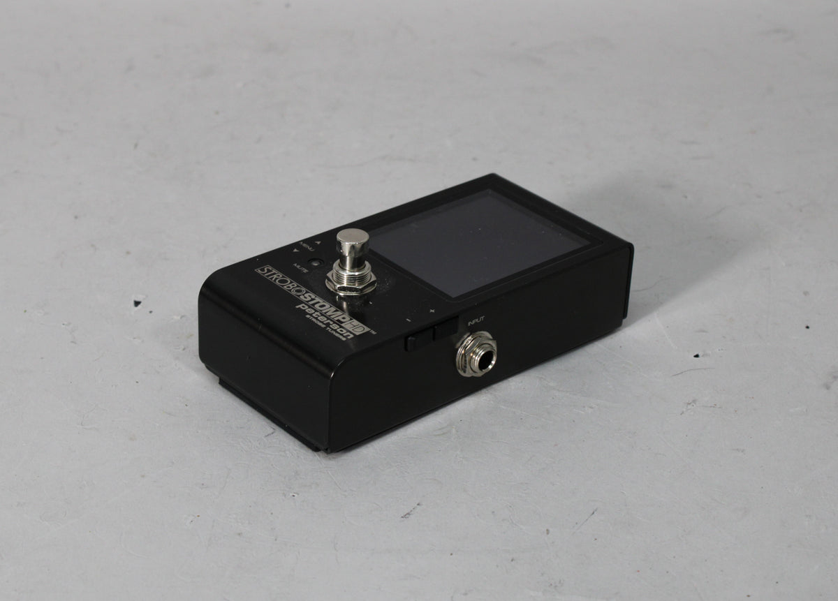 A black tuner pedal, angled from the right, showing the screen, footswitch, and input jack.
