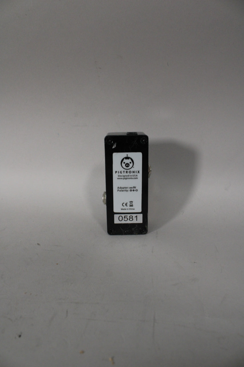 The black pedal is viewed from the back, showing a white label with text and a serial number, and two silver jacks on the sides.