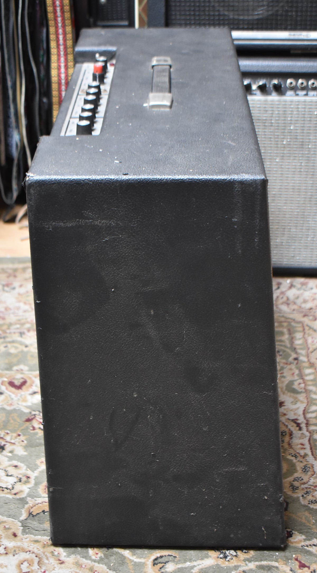 The black textured amp is viewed from the right side, showing the top handle, control panel with black knobs, and scuffs on the tolex.