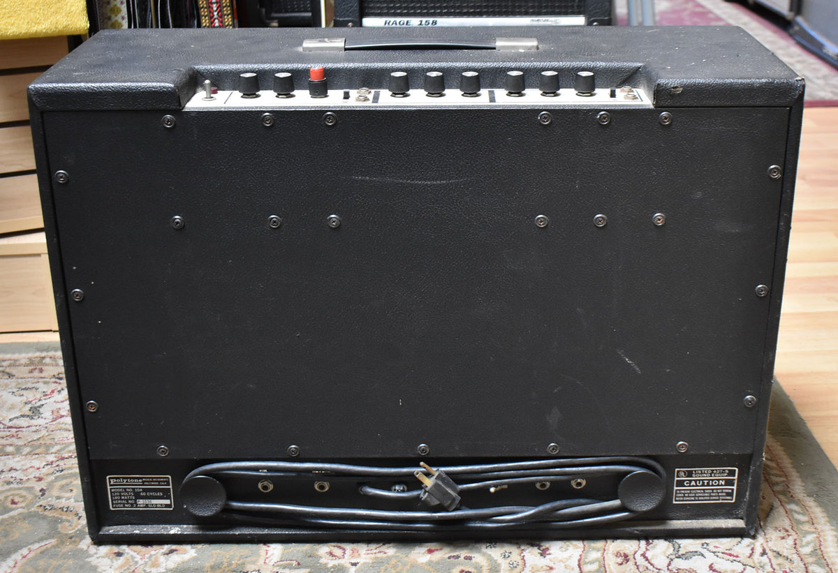 Rear view of a black textured combo amp with a top handle, control panel, and power cord wrapped at the bottom.
