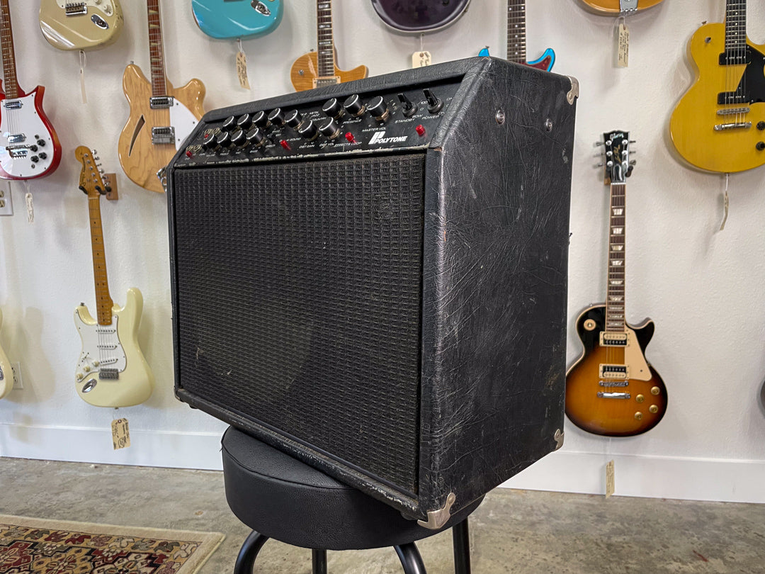 The black combo amp is angled right, showing its textured front grille, top control panel with many knobs, and worn side panel.