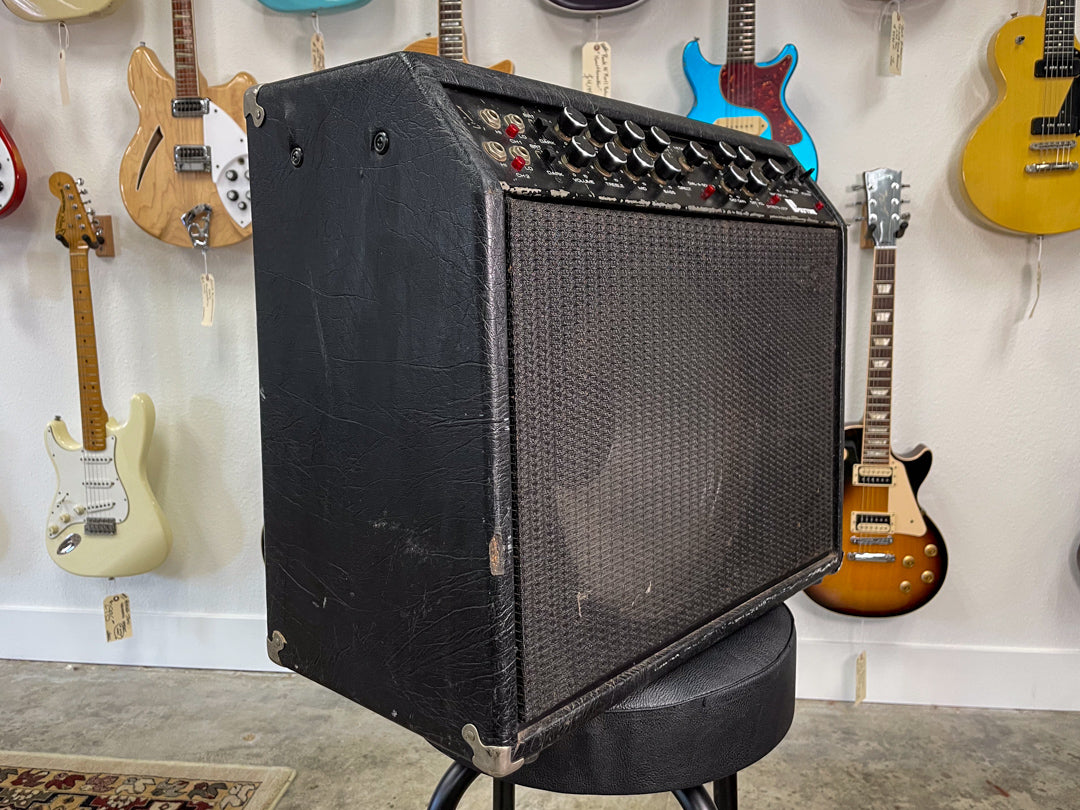 The black combo amp is angled right, showing its textured black tolex, metal corner protectors, and a full control panel.