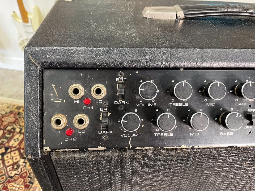 Close-up of the amp's black control panel, showing two channels of input jacks, toggle switches, and four large black rotary knobs.