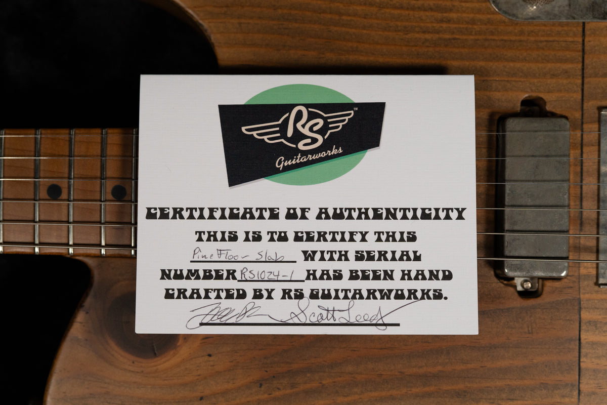 A white Certificate of Authenticity with a green and black logo rests on the guitar's dark brown body, partially covering the fretboard.