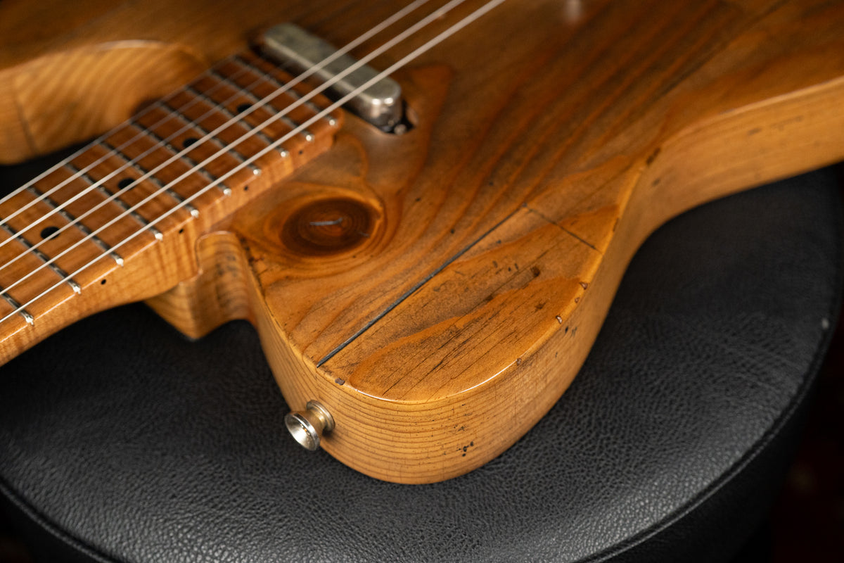 Close-up of the guitar's lower body, showing a prominent knot, dark grain lines, and a silver output jack on the light brown wood.