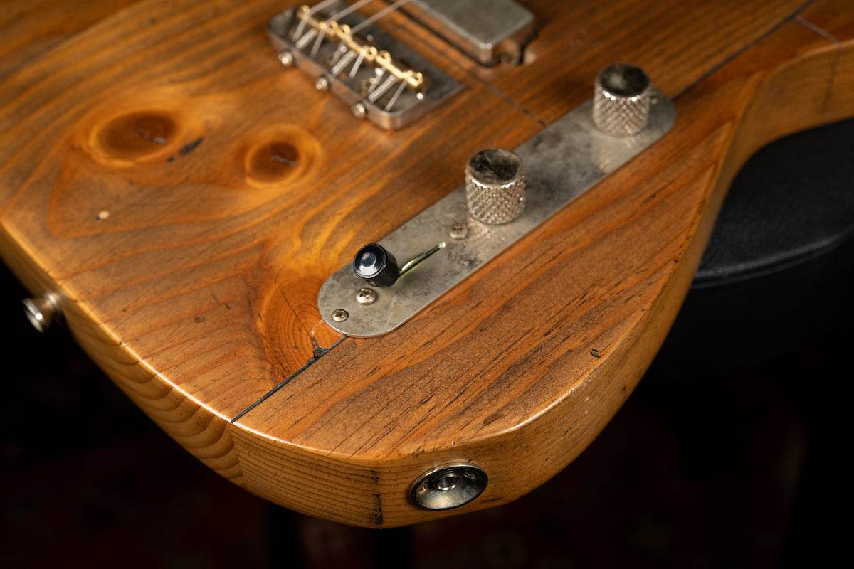 Close-up of the lower bout, showing the worn pine body with prominent knots, control plate with two knurled knobs, and output jack.