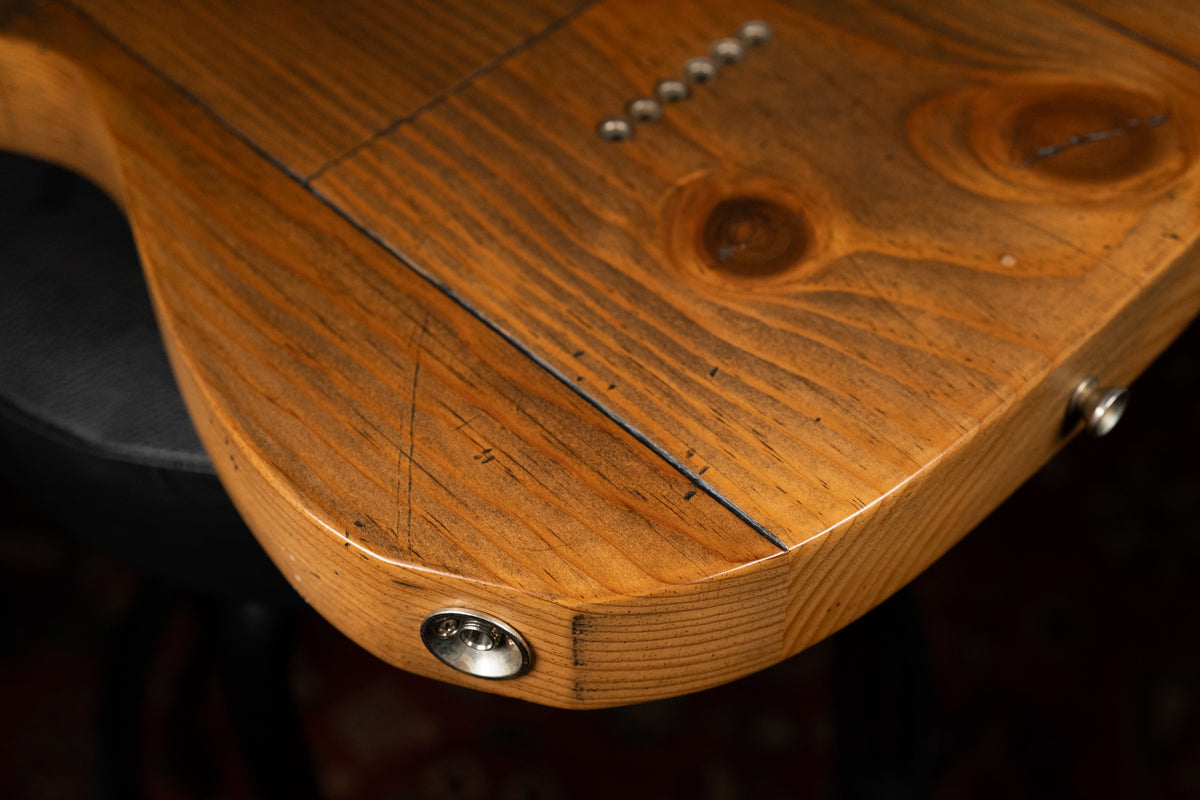Close-up of the guitar's lower body, showing the worn, light brown pine grain, a chrome output jack, and six string ferrules.