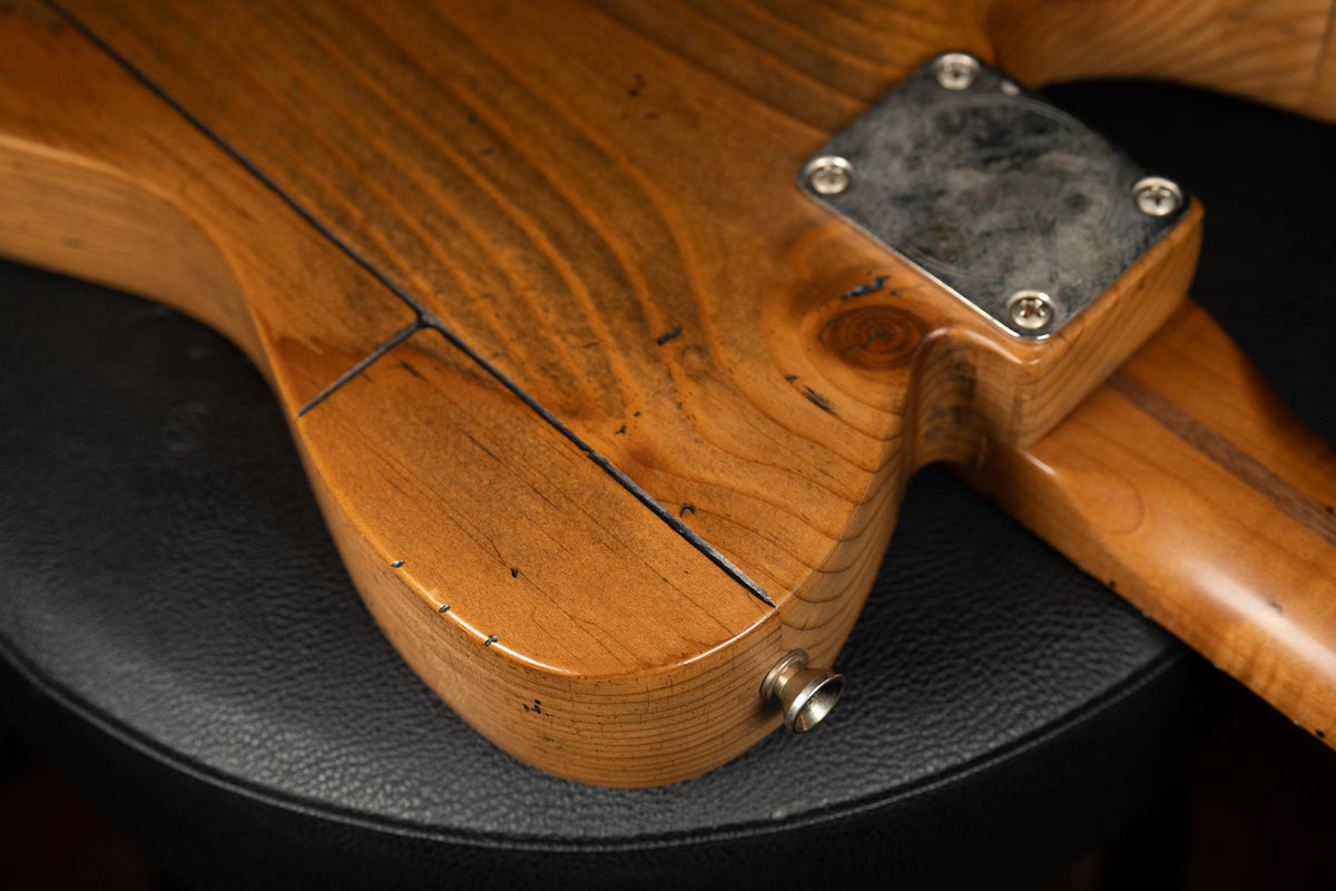 The guitar's lower body, viewed from the back, shows a worn, light brown pine finish with dark grain lines, a neck plate, and an output jack.