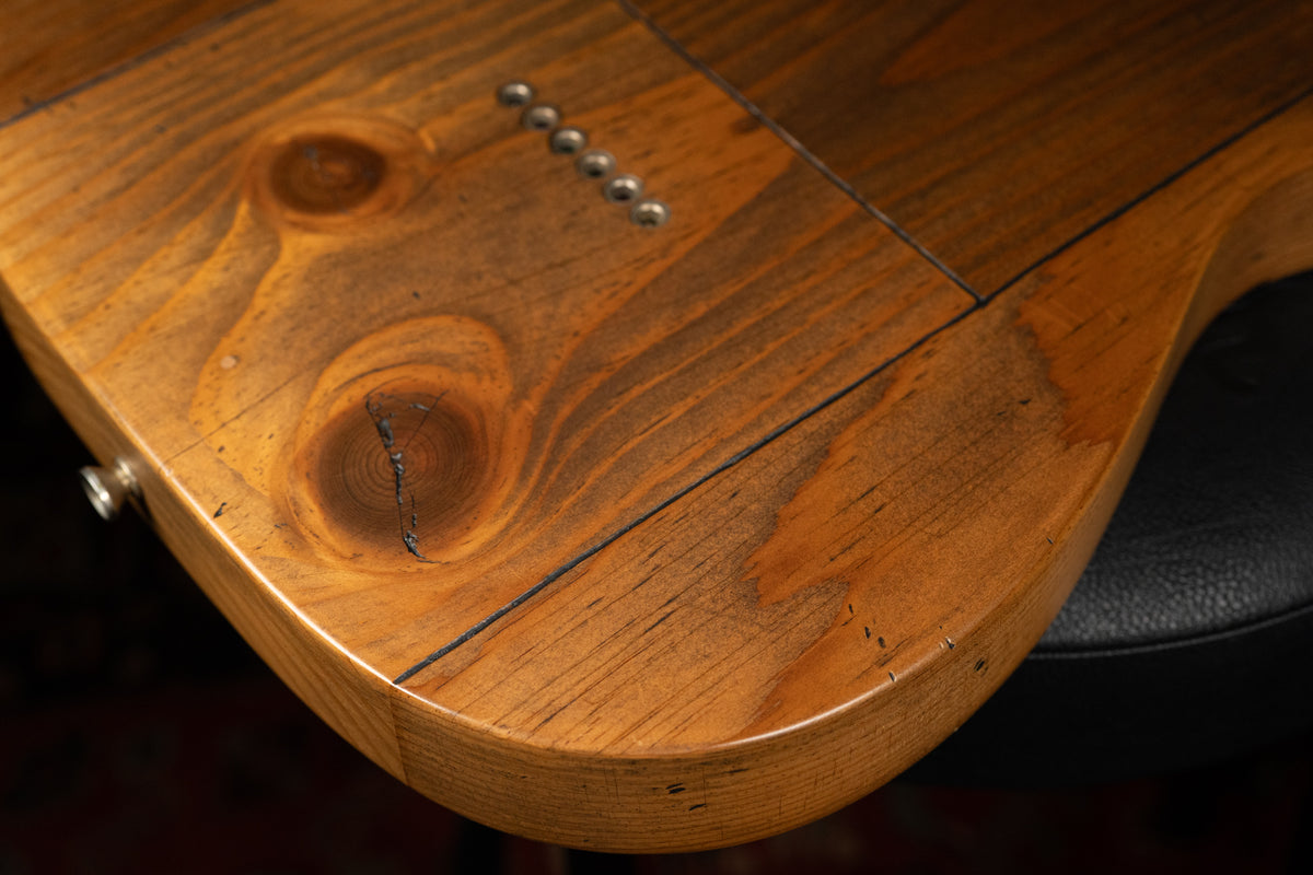 Close-up of the guitar's lower bout, showing a natural pine finish with prominent knots, cracks, and six string-through ferrules.