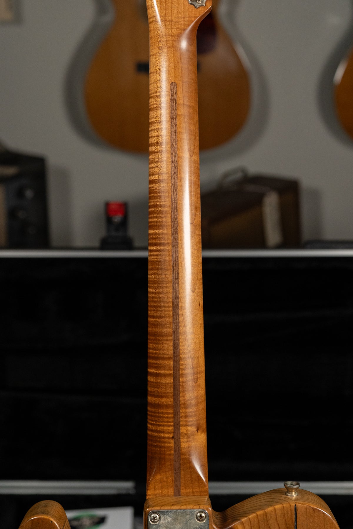 The back of a light brown guitar neck with a dark central stripe and flame maple figuring, viewed from the body.